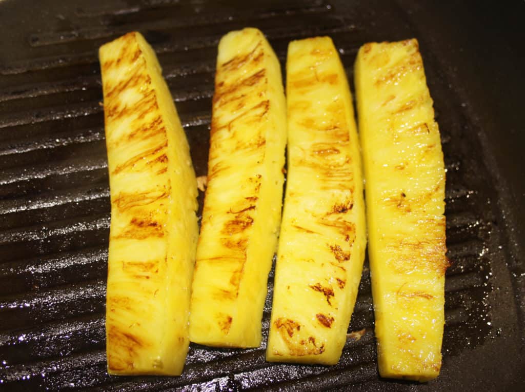 pineapple spears grilling in a griddle pan. 