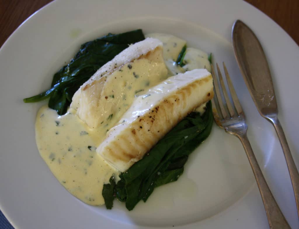 finished dish ofCod on a bed of spinach with a  sauce which is flavoured with basil.