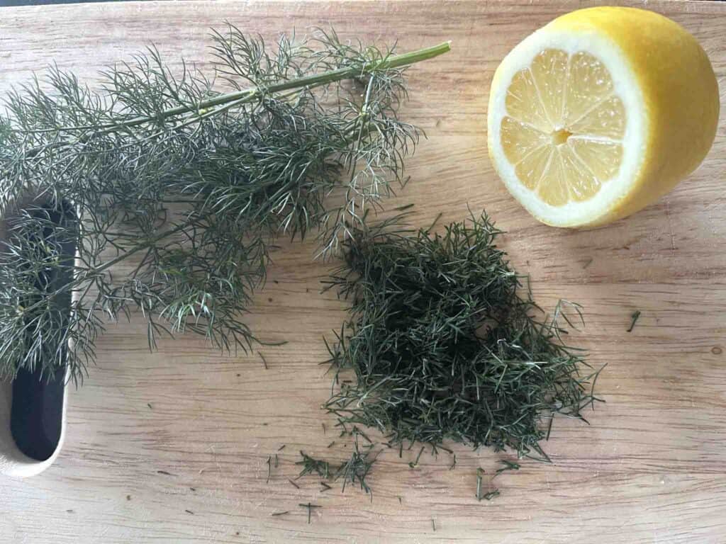 half a lemon and chopped dill on a board.