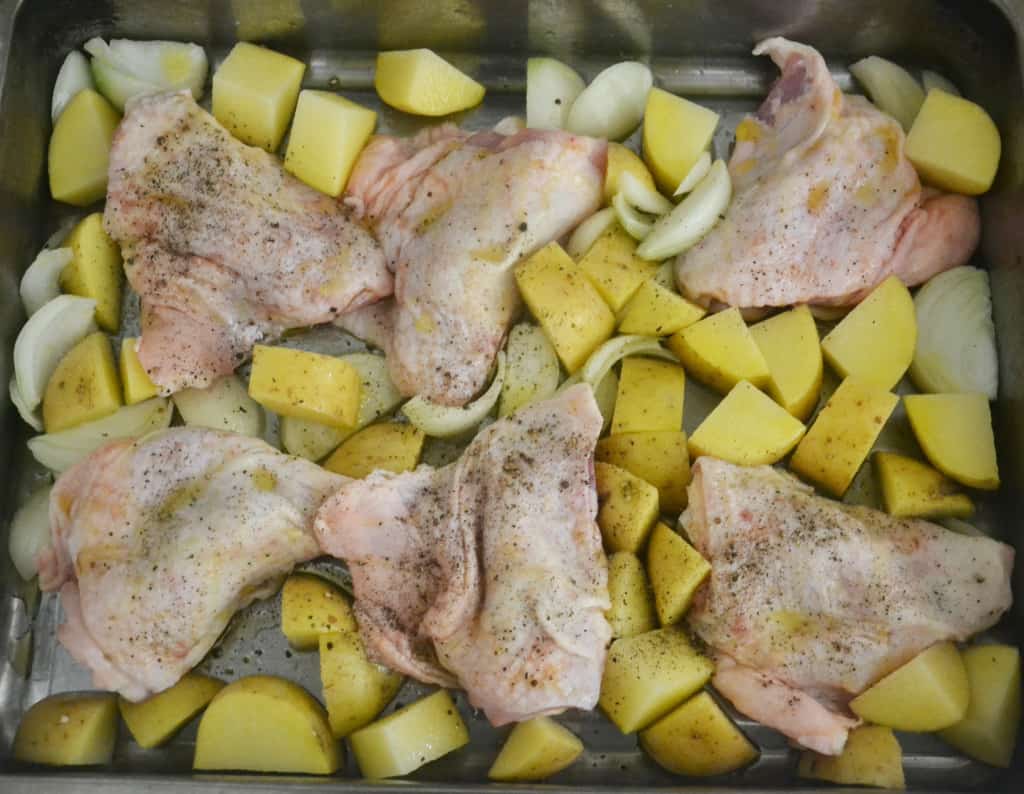 chicken thighs, potatoes and onion in a roasting dish.