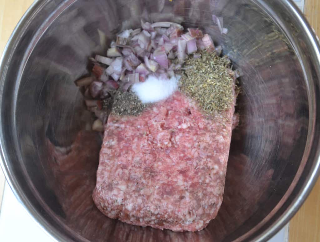 bowl filled with a block of mincemeat, shallots, herbs and seasoning.