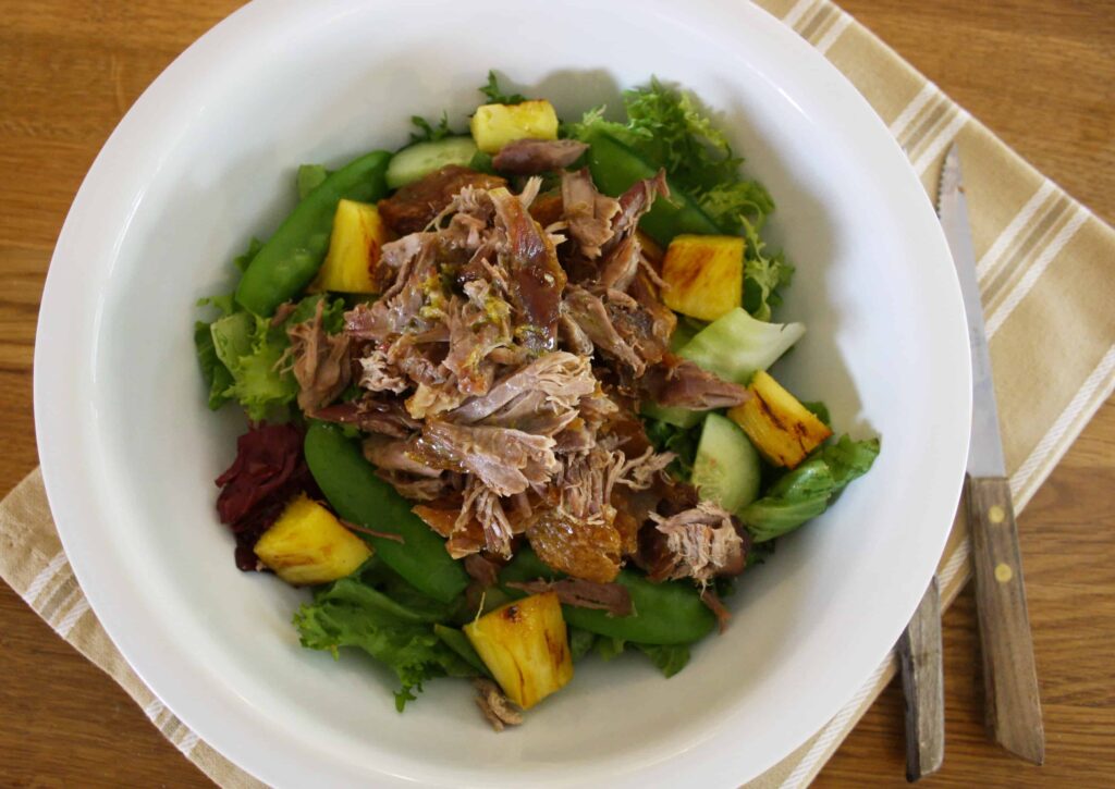 Warm confit duck salad in a bowl with a lemon and lime dressing. 