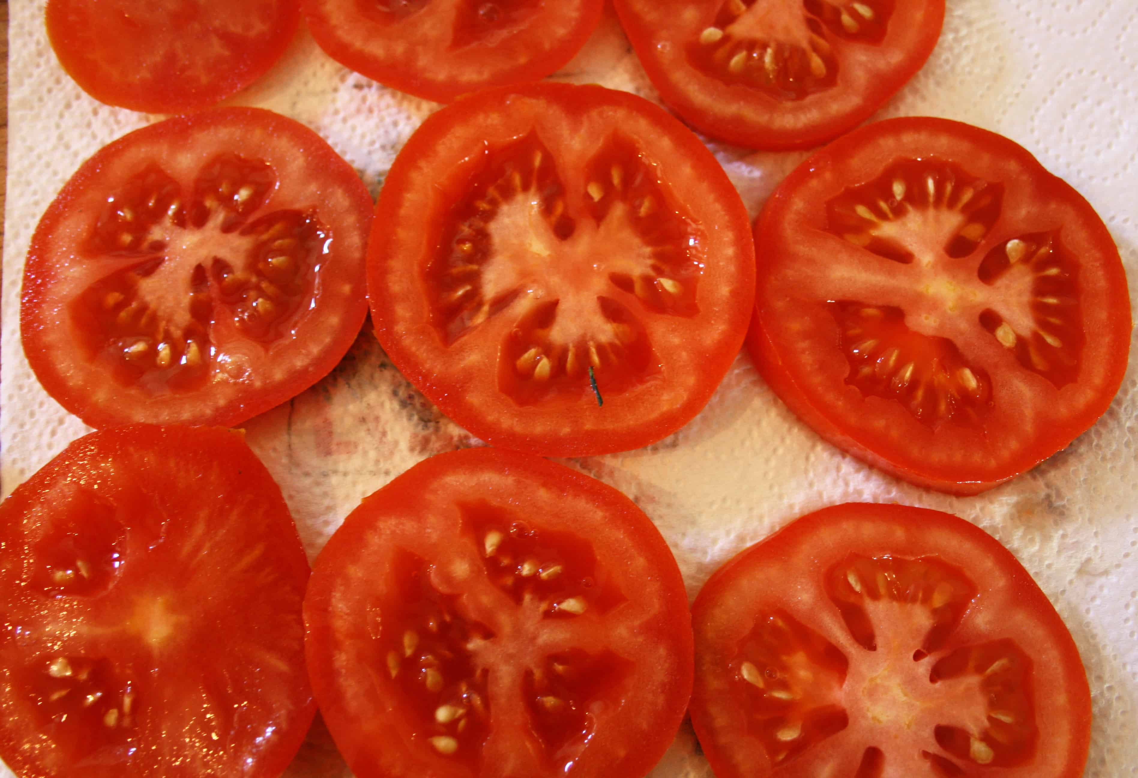 sliced tomatoes draining on kitchen towel.