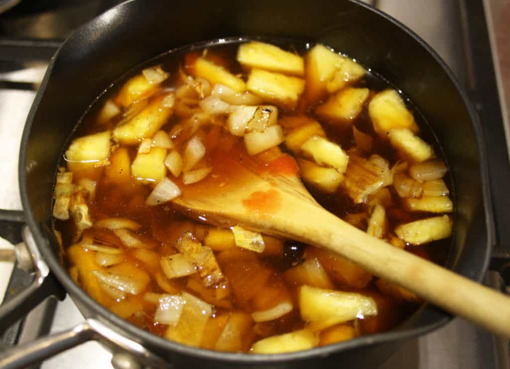 pineapply and sauce ingredients in a small saucepan with a wooden spoon.