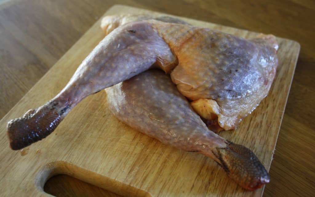 two guinea fowl legs on a chopping board.