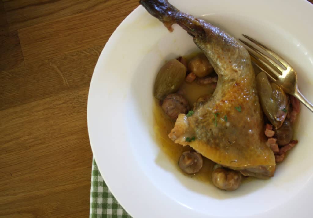 guinea fowl leg in a bowl with chestnuts and onions.