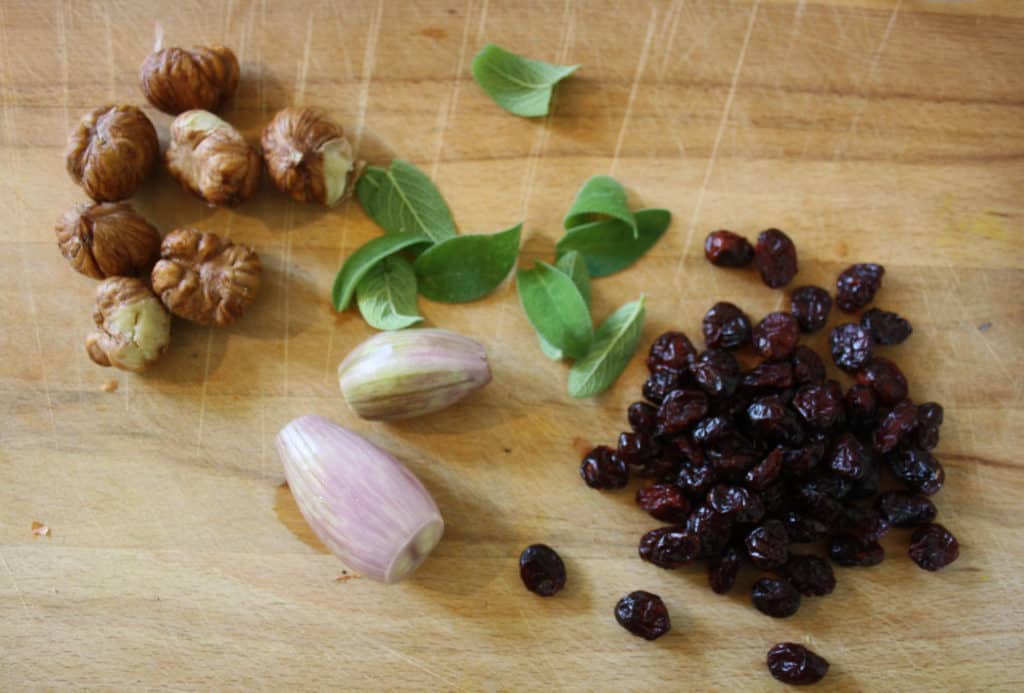chestnuts, cranberries, sage leaves and shallots on a chopping board.
