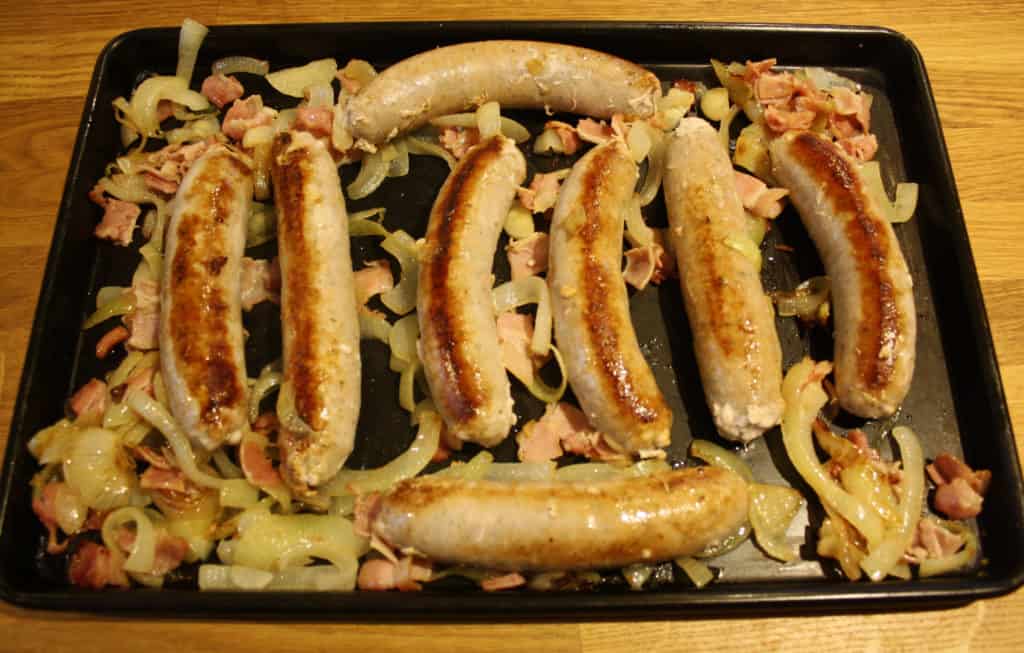 Browned sausages on a roasting dish with onions and bacon