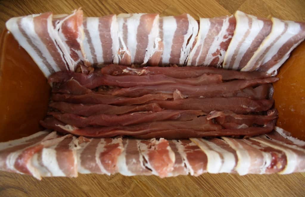 dish lined with bacon and showing a layer of duck fillets.