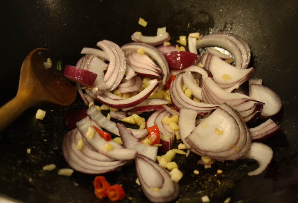 wok with red onions, garlic, chilli and ginger frying.