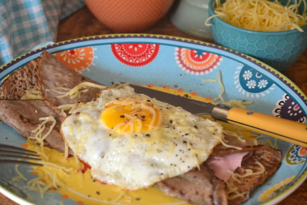 savoury pancake folded on a plate with a fried egg on top.