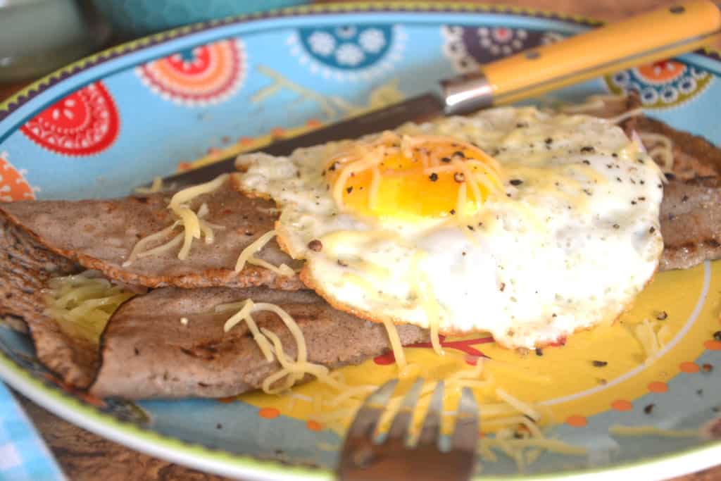 savoury pancake folded on a plate with a fried egg on top.