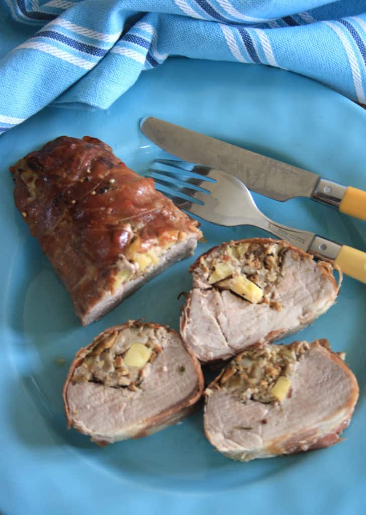 bacon wrapped stuffed pork fillet or tenderloin with 3 slices cut on a plate with cutlery.
