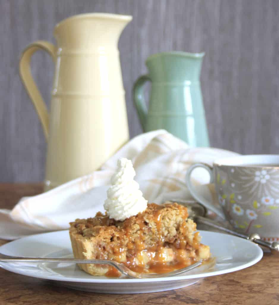 Slice of salted caramel apple crumble tart, topped with cream with jugs in the background