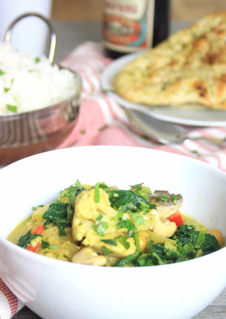 bowl of curry with rice and naan in the background
