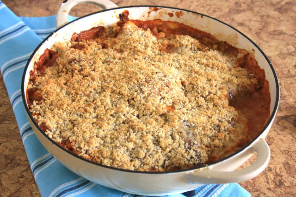 large casserole dish of chicken in tomato and beans with breadcrumb topping on a tea towel.
