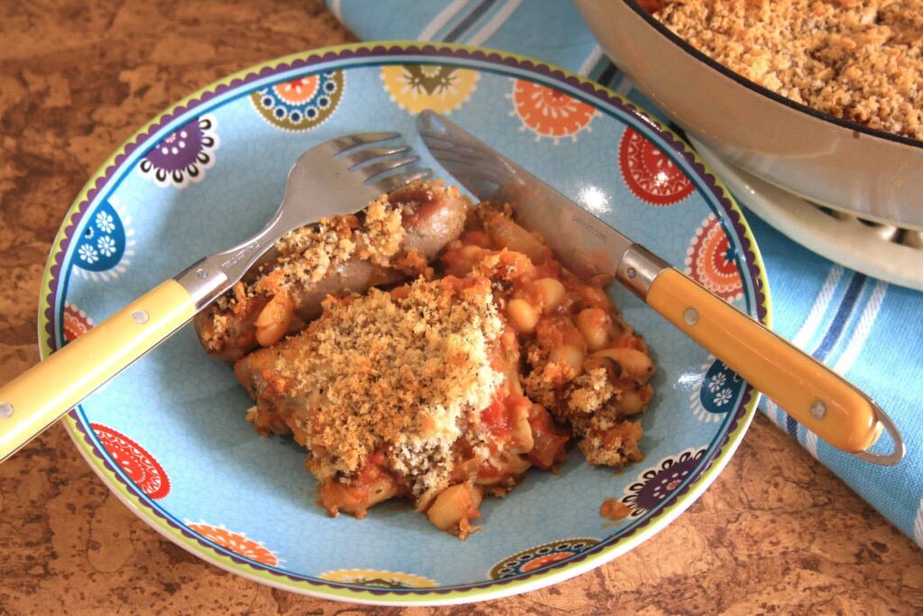 chicken, sasauge and beans in a bowl with a knife and fork.
 