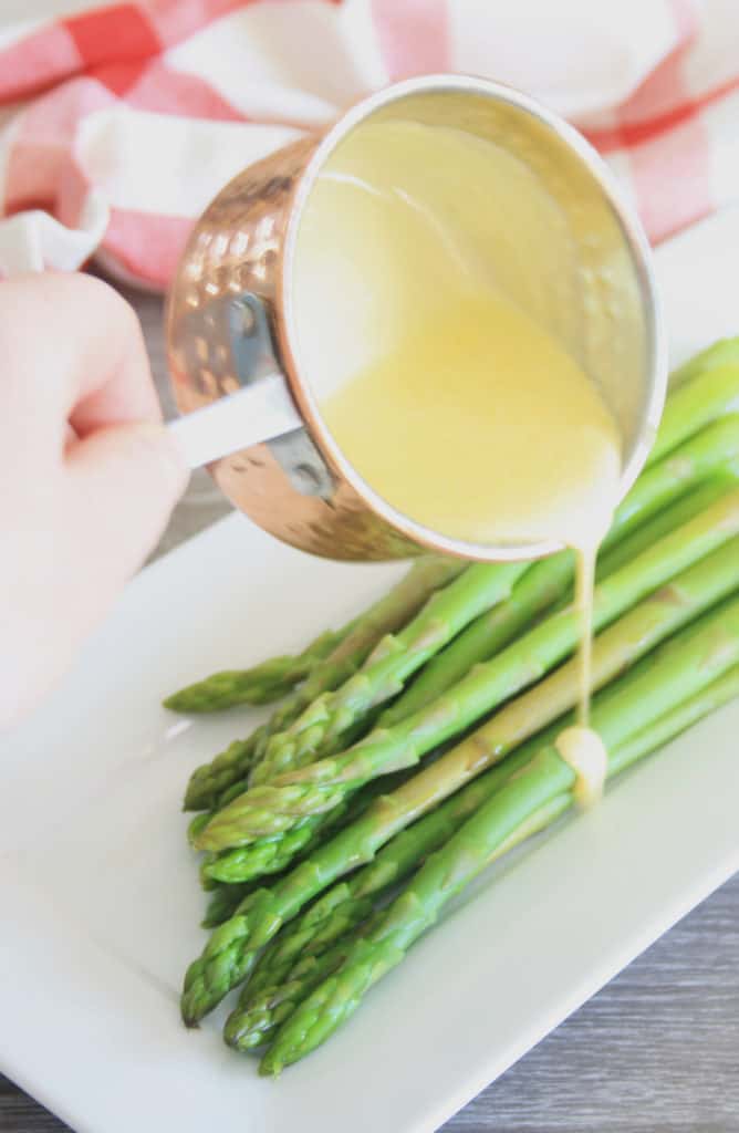 Hollandaise poured from a pan onto asparagus