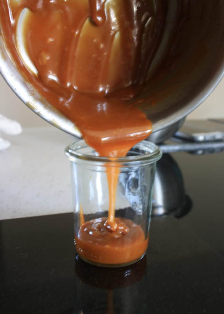 caramel sauce pouring from a saucepan into a glass jar.