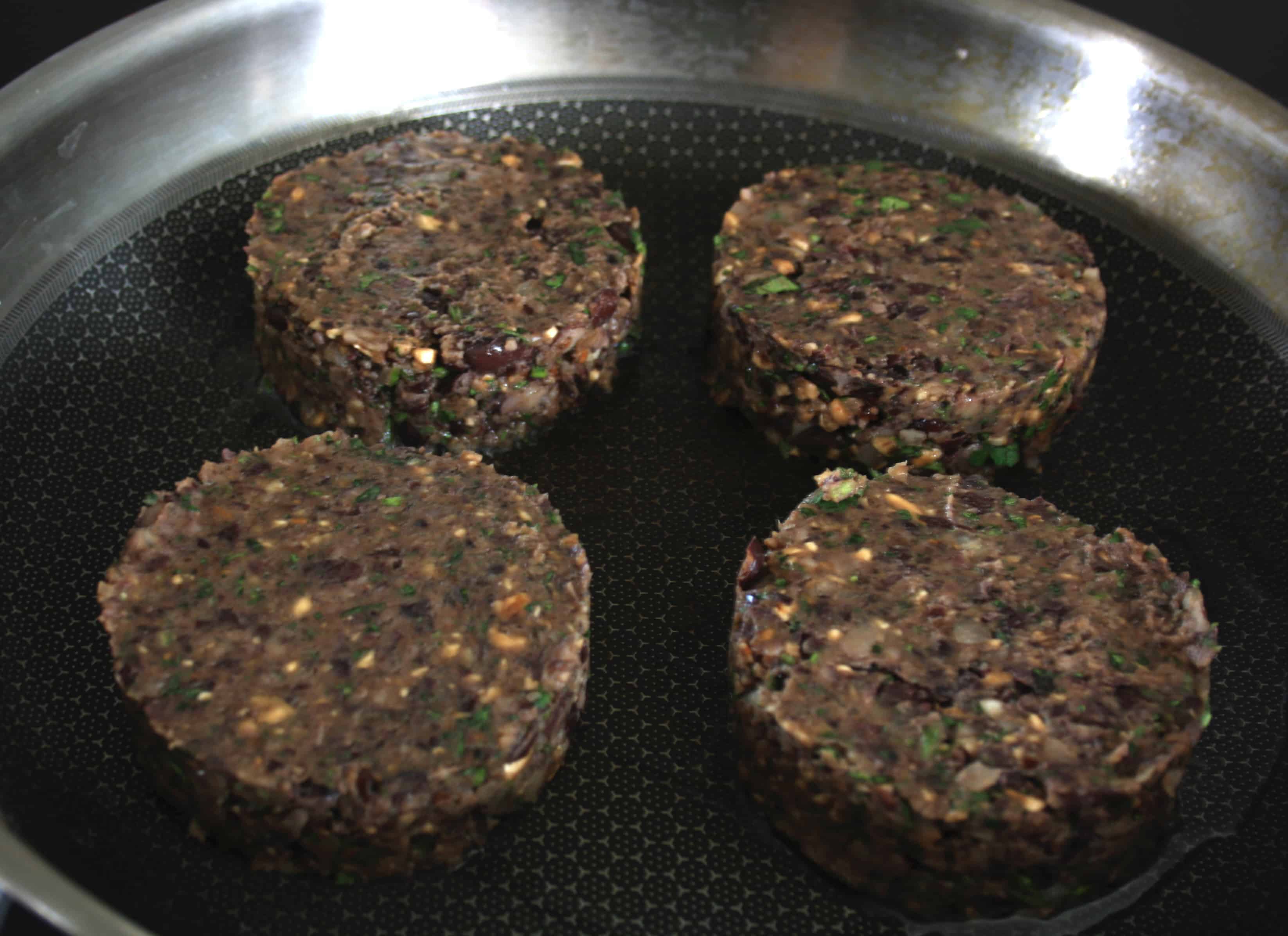 four mushroom burgers in a frying pan.