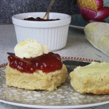 scone with jam and cream on top and pot of jam in background