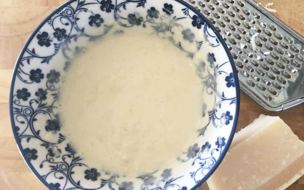 homemade dressing in a bowl with Parmesan cheese and a grater