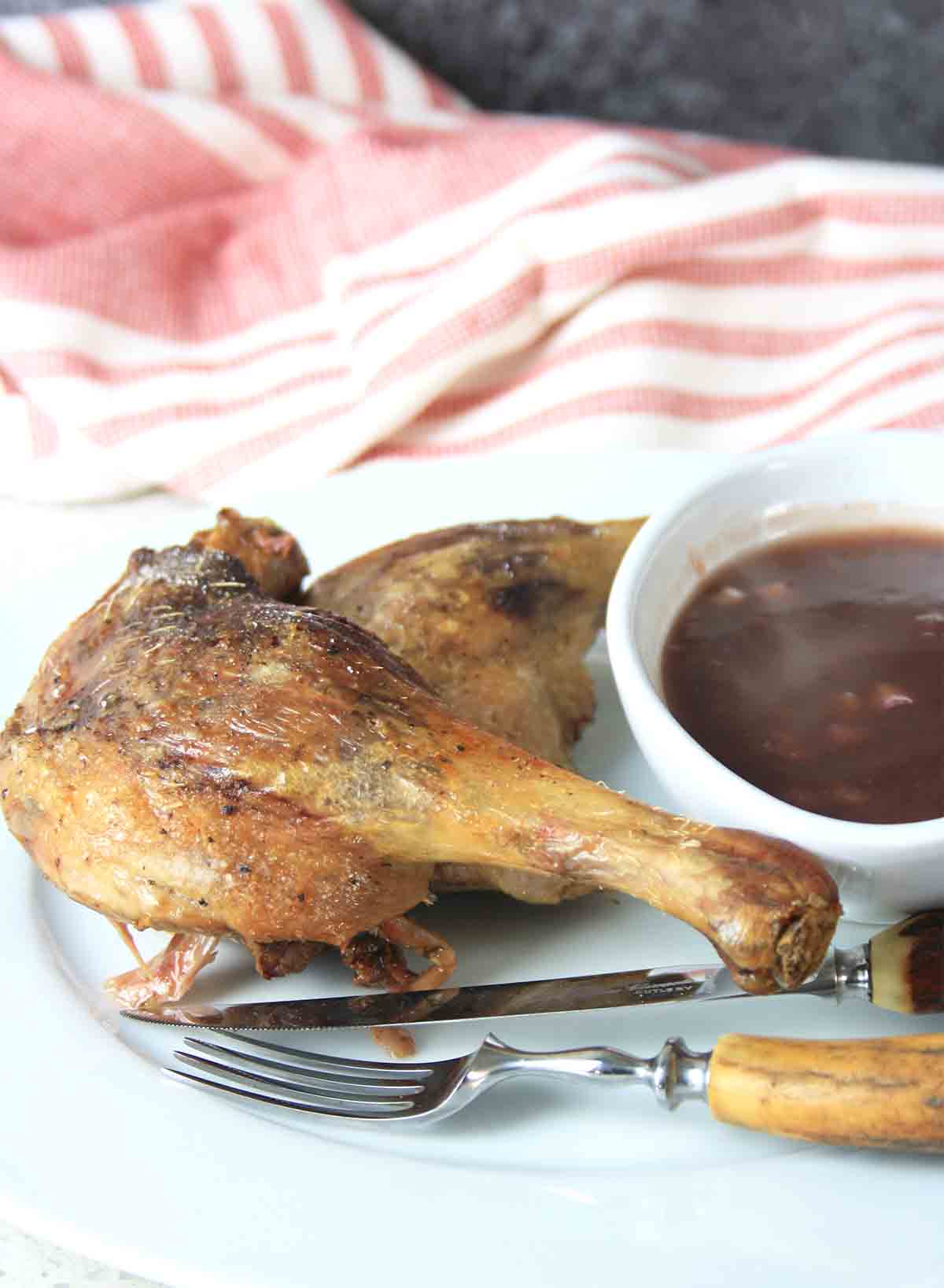 duck confit with pot of sauce and cutlery.