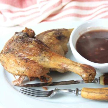 duck legs with redcurrant sauce in a bowl with a knife and fork.