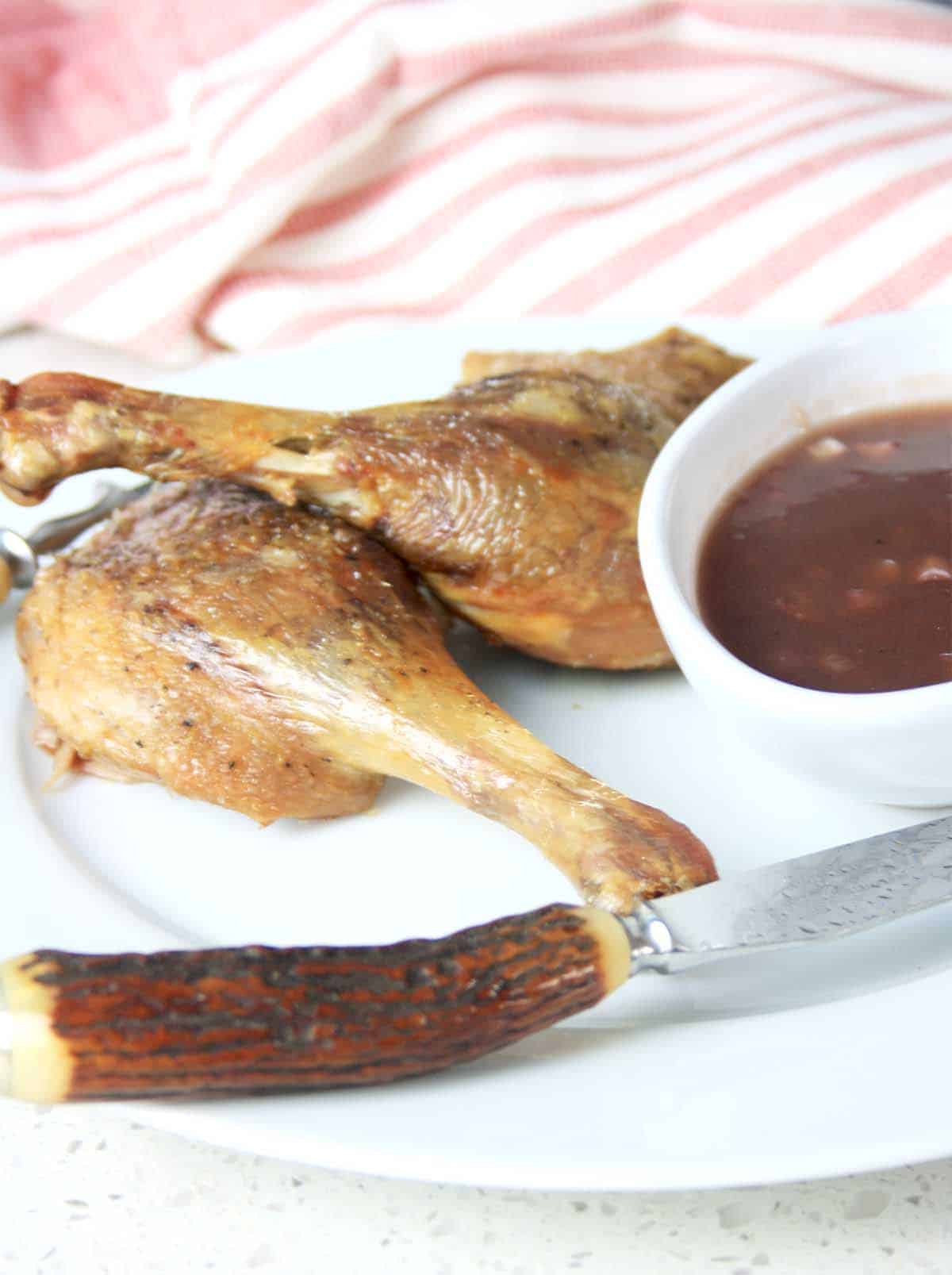 two duck legs on a plate with a pot of sauce