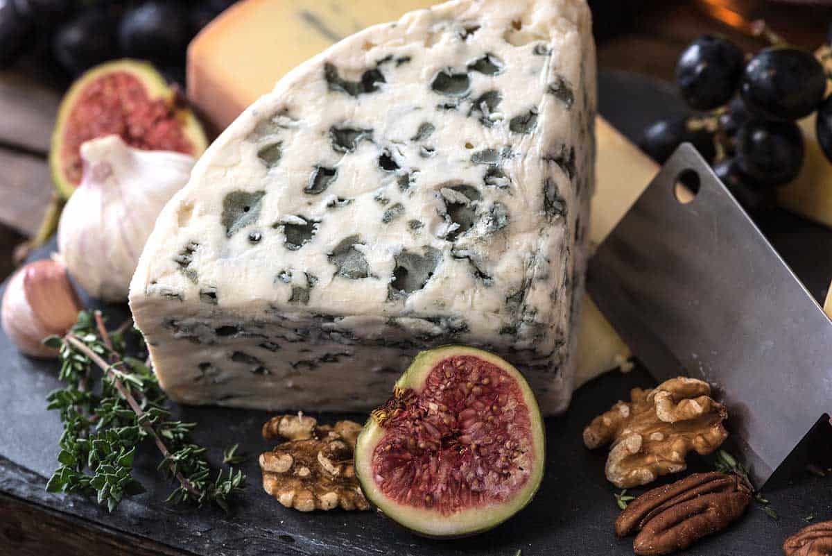 big wedge of blue cheese surrounded by nuts and fruit.