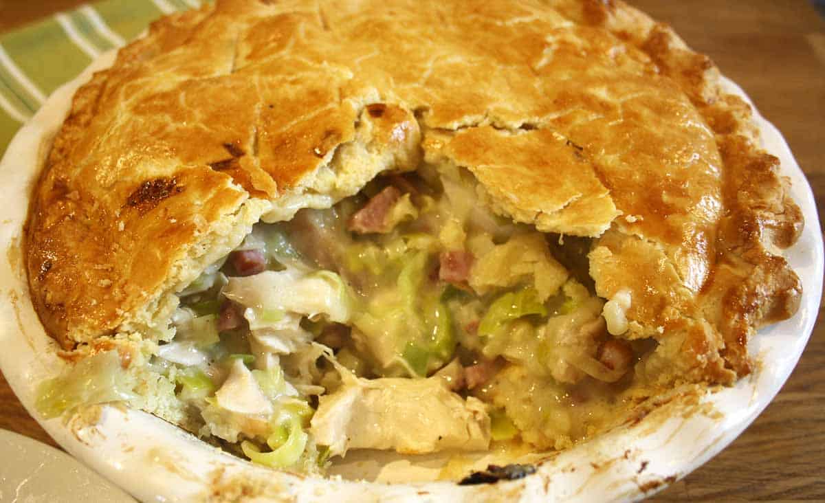 chicken and ham or bacon leek pie with bacon with a portion cut out.