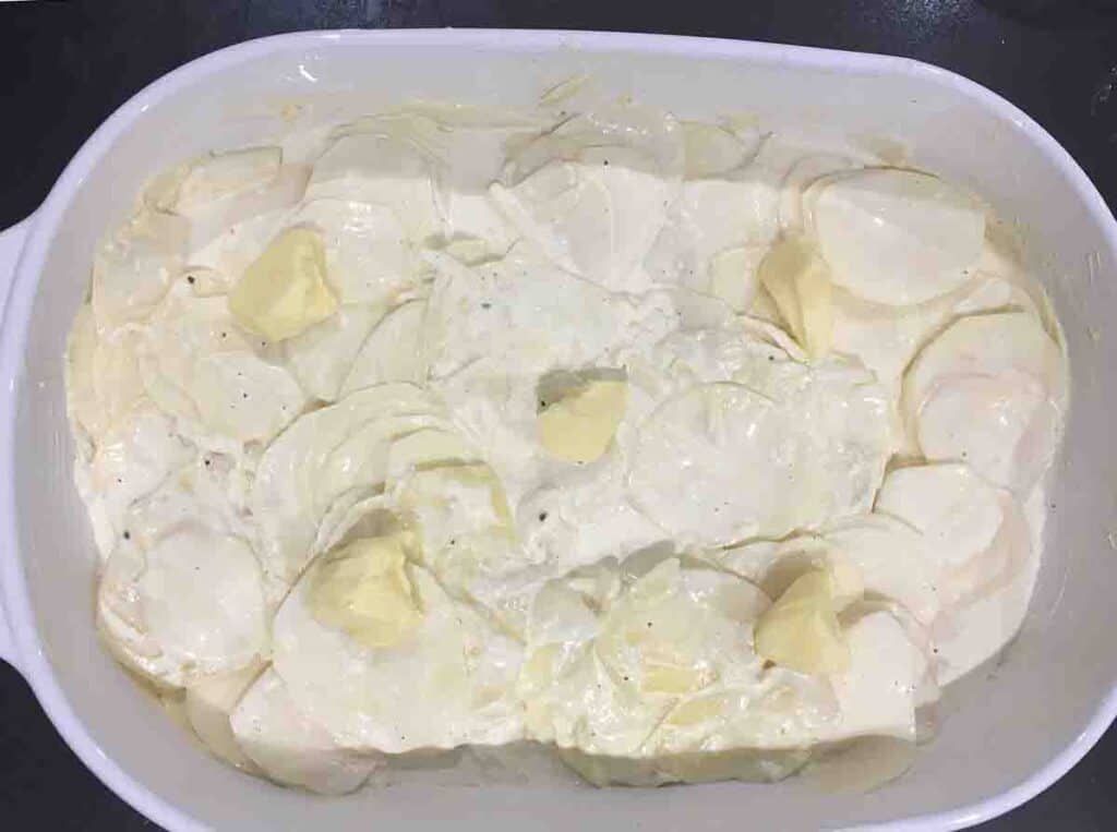 cream and potatoes in a baking dish with lumps of butter on the surface.