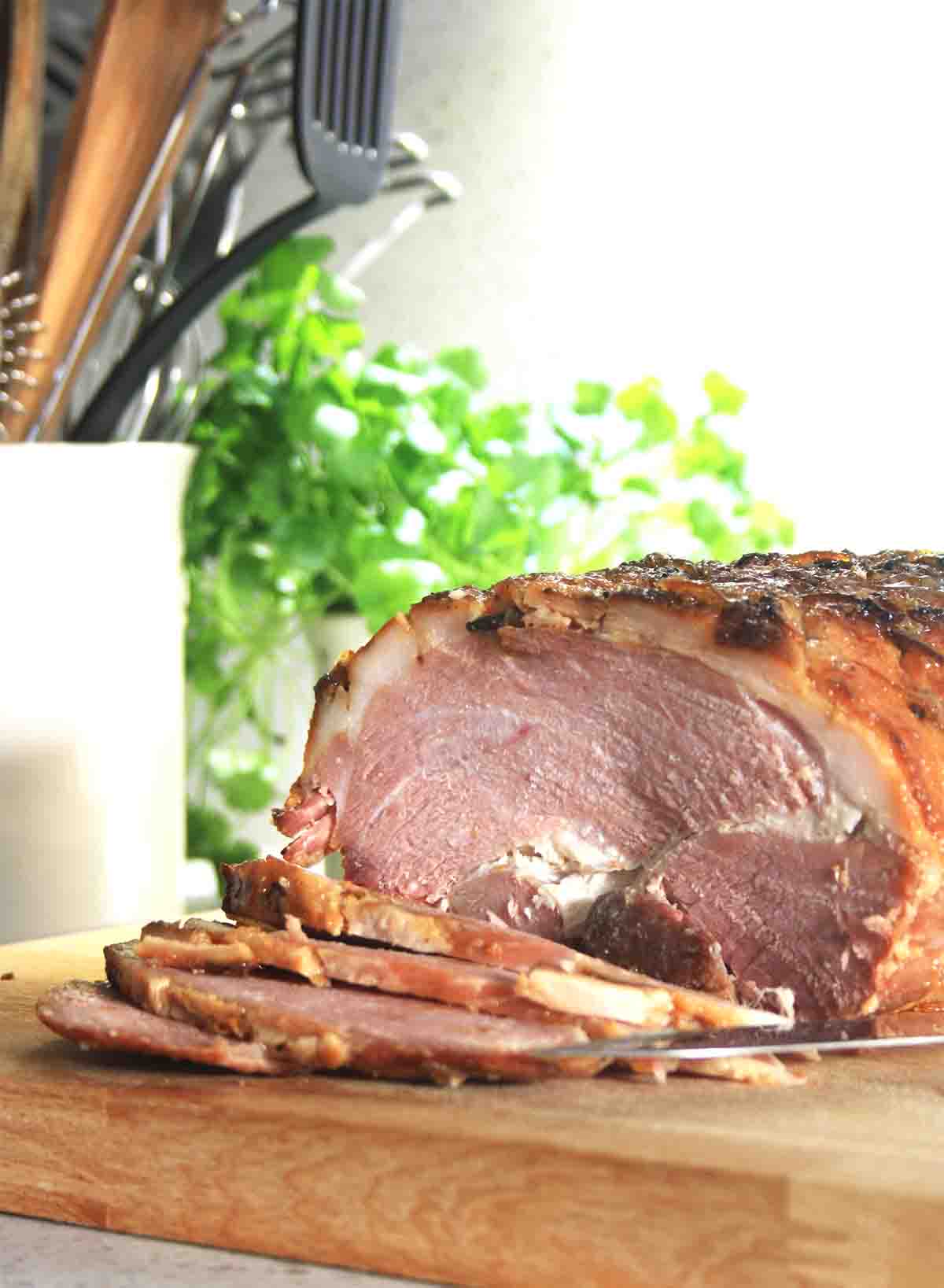 bourbon glazed ham with slices cut and utensils in the background.
