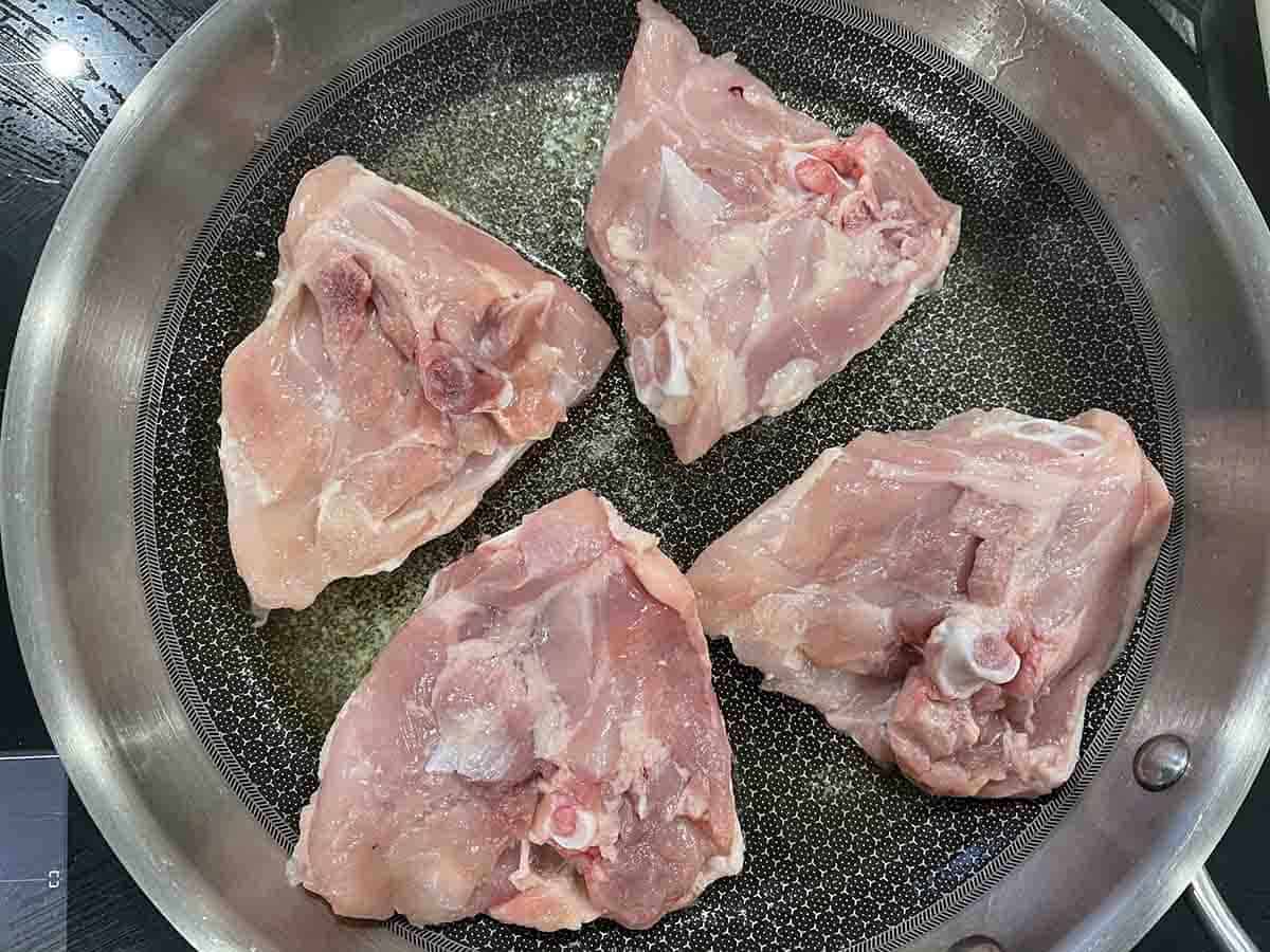 chicken thighs skin side down in a frying pan.