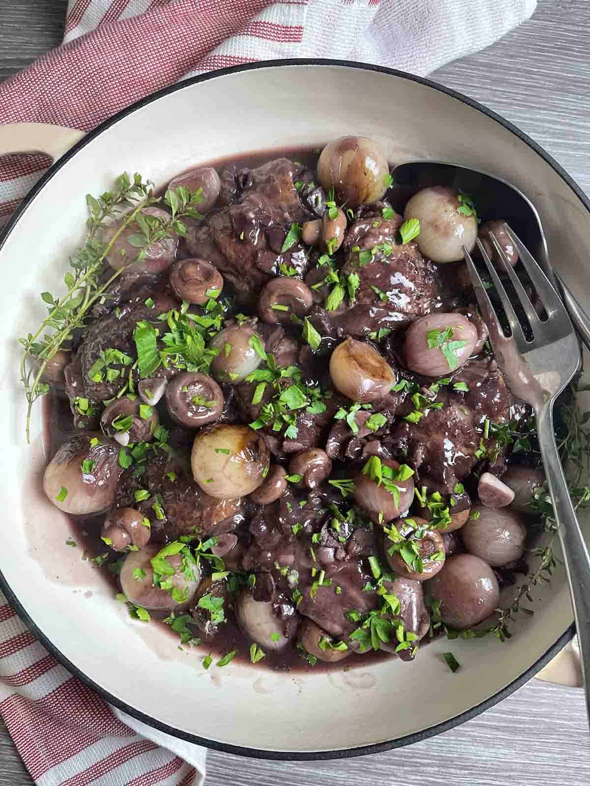 traditional coq au vin or French chicken in red wine in a round casserole dish with a fork.