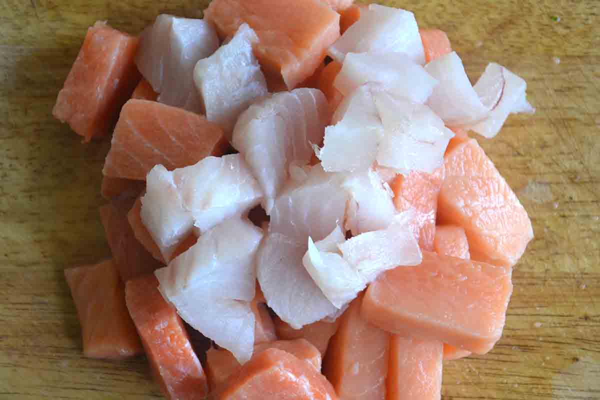 salmon and white fish cut into cubes in a pile on a wooden chopping board.
