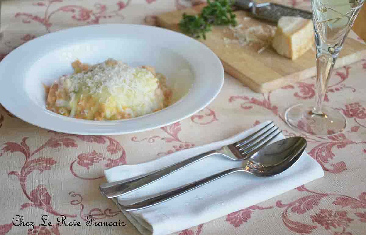 portion of pasta dish in a bowl with parmesan cheese, grater and cutlery to the right.