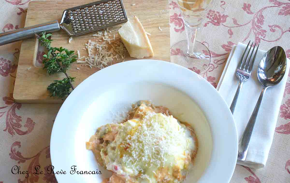 portion of pasta dish in a bowl with parmesan cheese and grater to the left and cutlery to the right.