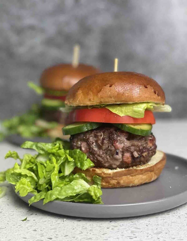 venison burger in a bun with cucumber and peppers on a plate with salad on the side.