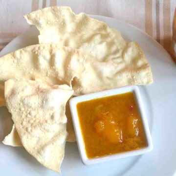 poppadums om a plate with small pot of spicy mango chutney with lime.