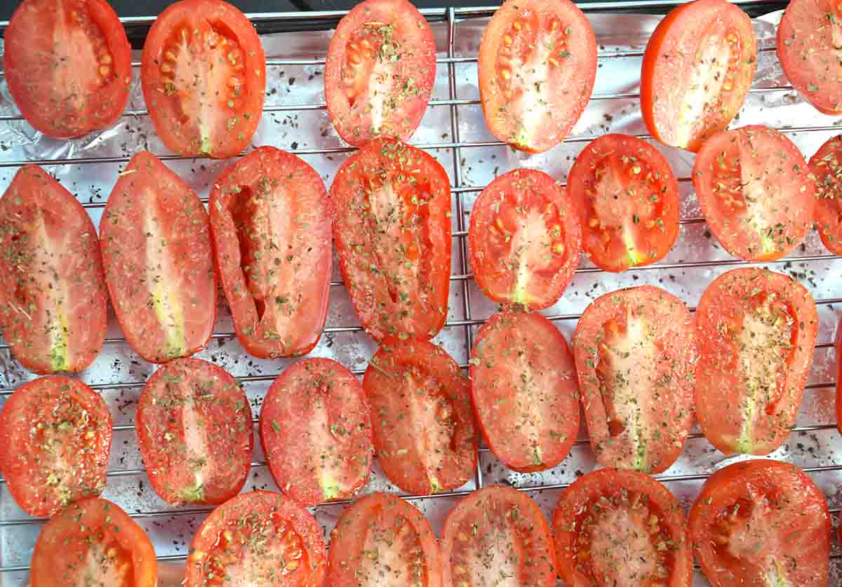 raw tomatoes sliced in half, cut side up on a grill rack.