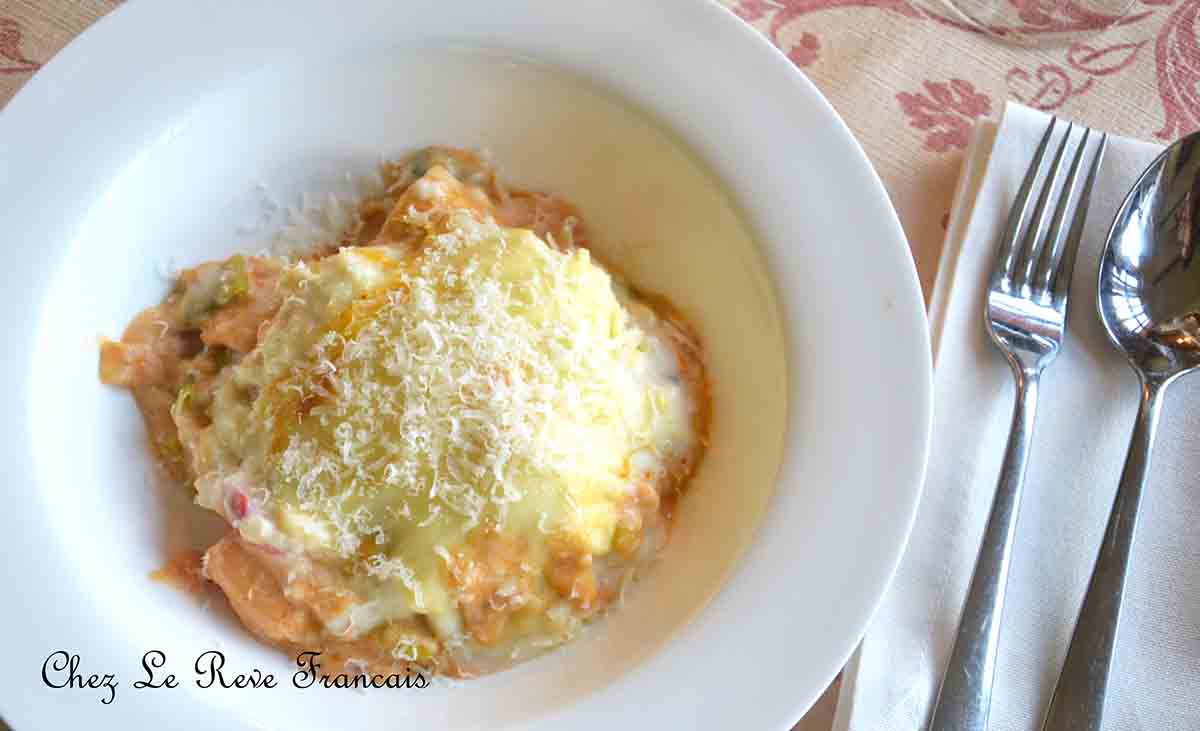 portion of seafood lasagne in a shallow bowl with a spoon and fork on the right side.