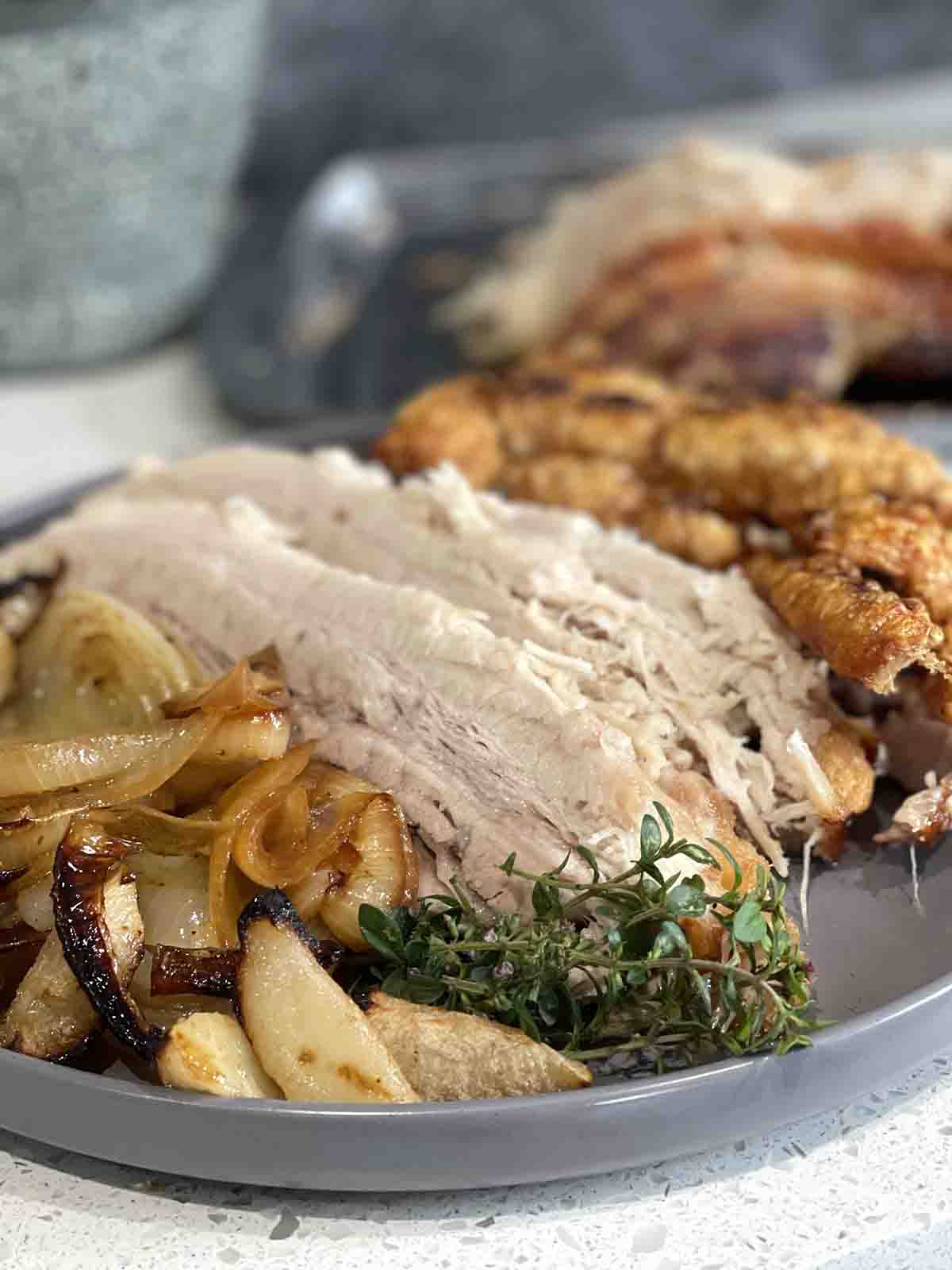 slow roast belly pork in slices with crackling in the background and onions and apples in front. Great for Easter roasts.