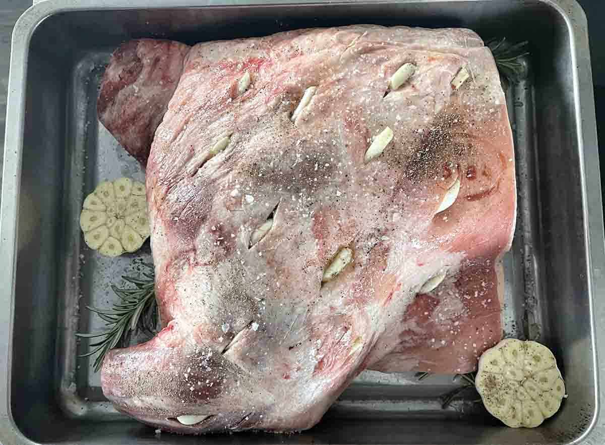 lamb in roasting pan with slits cut stuffed with garlic and rosemary.
