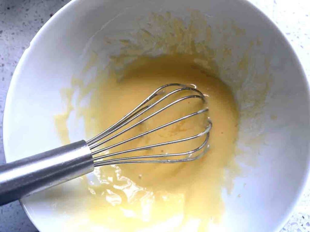 Egg yolks in a bowl with a whisk.