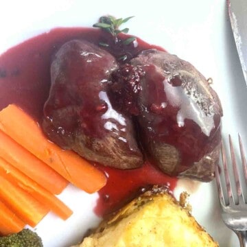 two pan fried pigeon breast covered with b;ackberry sauce on a plate with carrots and potatoes gratin.