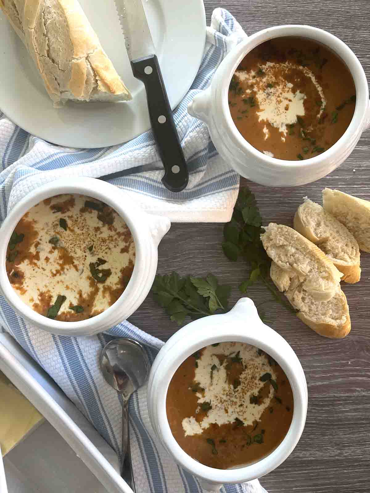 three bowls of fish soup with  cut bread on plates.