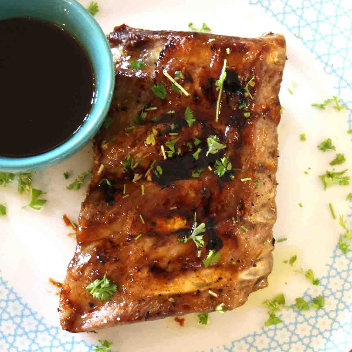 sticky bourbon ribs on a plate with sauce in a pot.