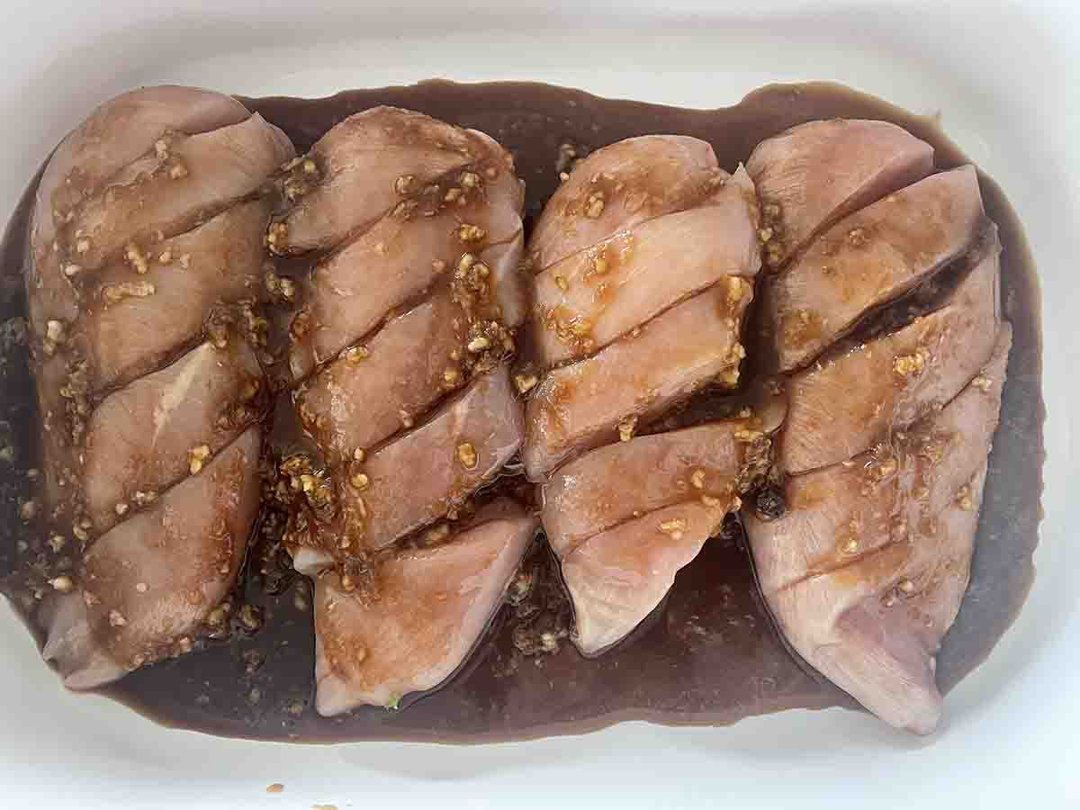 raw chicken breasts in a dish with marinade poured over.