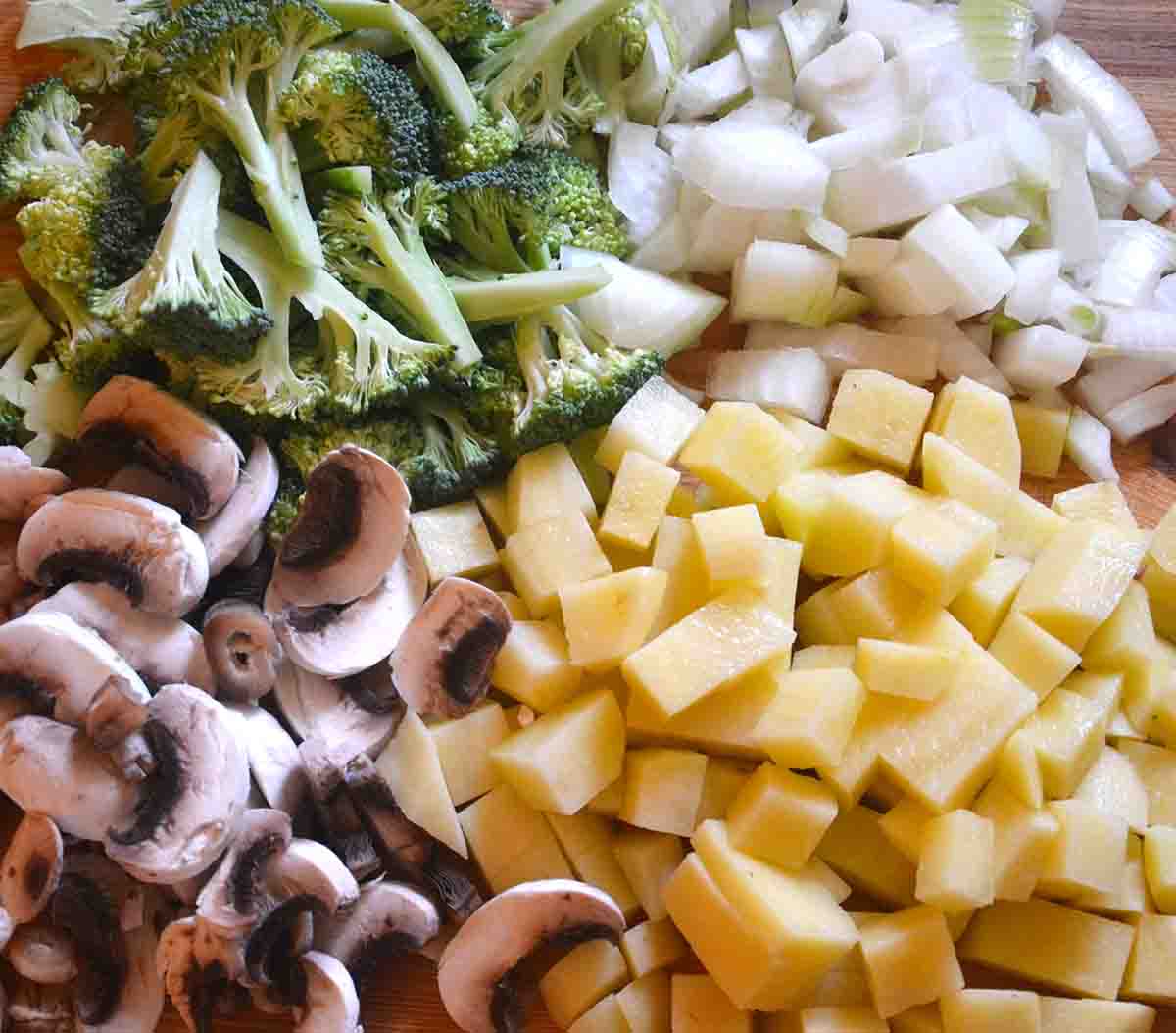 chopped broccoli, mushrooms and potatoes on a board.